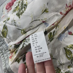 Peut inclure: Gros plan sur la doublure int&eacute;rieure d'un v&ecirc;tement, avec un motif floral dans les tons de rouge, vert et bleu sur fond cr&egrave;me. Une &eacute;tiquette avec du texte en plusieurs langues est visible, indiquant la composition du mat&eacute;riau et les instructions d'entretien.