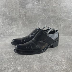 以下が含まれることがあります： 滑らかで光沢のある仕上げの黒いレザー製スリッポンシューズ。丸みを帯びたトゥ、低いブロックヒール、甲部分にフィット感を高める幅広の伸縮性パネルを備えています。シューズ内部にはシルバーカラーの金属製シューキーパーが入っています。