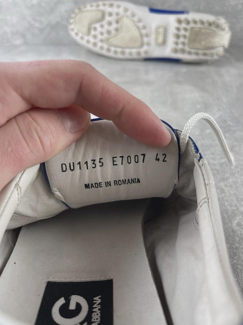 May include: White leather shoe with blue trim and white laces. The shoe's interior displays the text "DU1135 E7007 42" and "MADE IN ROMANIA". The sole is white with a blue accent.