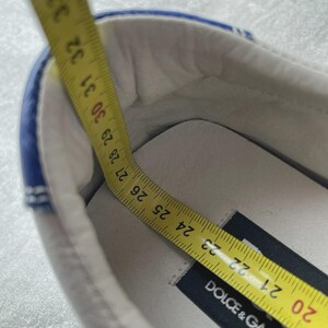 May include: White shoe with blue trim, measured with a yellow tape measure. The tape measure shows a length of approximately 23 cm. The shoe has a black label that reads "DOLCE & GABBANA".