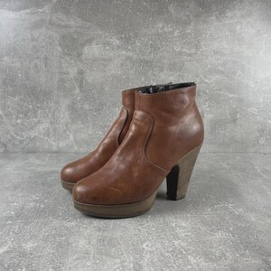 May include: A pair of brown leather ankle boots with a platform sole and wooden block heels. The boots have a side zipper and a rounded toe. The heels are approximately 4 inches high.