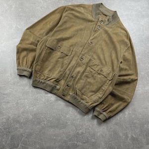 May include: A tan suede bomber jacket with a button-up front, two front pockets, and ribbed cuffs and collar. The jacket has a relaxed fit and a vintage aesthetic. The jacket is a size medium.