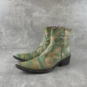 May include: A pair of ankle boots featuring a pointed toe and a low block heel. The boots are crafted with a textured, reptilian-like pattern in alternating shades of muted green and tan, with a side zip closure and a structured shaft.