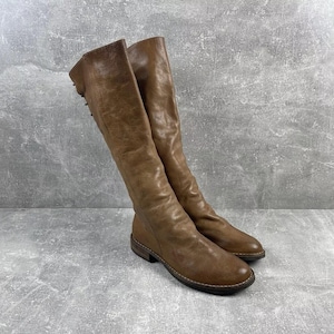 May include: A pair of knee-high brown leather boots. The boots have a worn, textured appearance and a low heel. The shaft of the boots is slightly slouchy, and the overall design is classic and versatile. The boots are suitable for various occasions.