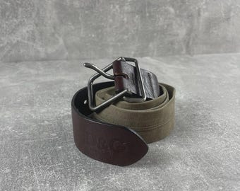 May include: A rolled-up belt with a brown leather tip and a silver buckle. The belt's main body is olive green canvas. The leather tip is embossed with the letters "D&G".