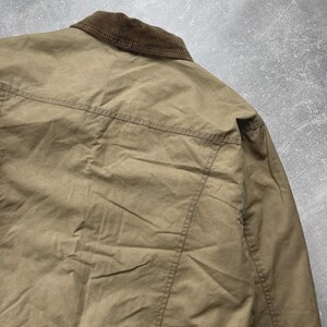 Puede incluir: Una chaqueta de color tostado con cuello de pana marr&oacute;n y una costura horizontal en la parte superior de la espalda. La prenda est&aacute; confeccionada en un tejido liso y mate con detalles de costuras visibles en los hombros y la espalda.