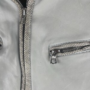 Peut inclure: Veste en cuir gris clair avec garniture &agrave; motif peau de serpent et d&eacute;tails zipp&eacute;s argent&eacute;s. La veste est dot&eacute;e d'une fermeture &eacute;clair et d'une petite poche zipp&eacute;e. Design classique.