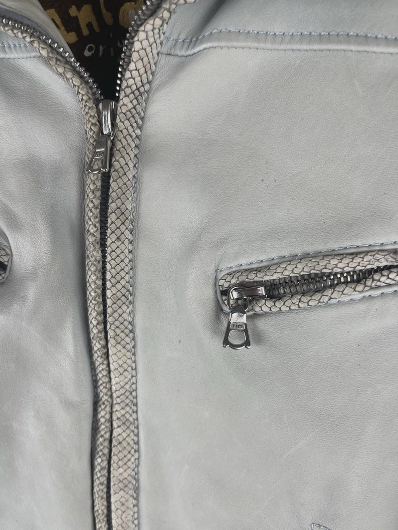 Peut inclure: Veste en cuir gris clair avec garniture &agrave; motif peau de serpent et d&eacute;tails zipp&eacute;s argent&eacute;s. La veste est dot&eacute;e d'une fermeture &eacute;clair et d'une petite poche zipp&eacute;e. Design classique.