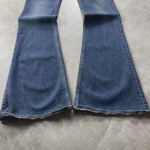 May include: A pair of blue denim jeans featuring a flared leg silhouette. The fabric displays a medium wash with subtle fading along the thighs and knees. The jeans have visible stitching along the seams and a classic hem at the bottom of each leg.