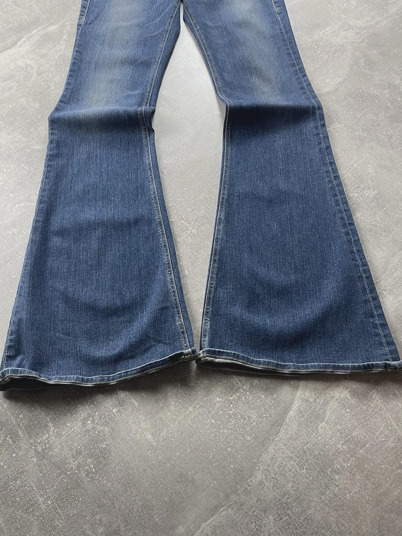 May include: A pair of blue denim jeans featuring a flared leg silhouette. The fabric displays a medium wash with subtle fading along the thighs and knees. The jeans have visible stitching along the seams and a classic hem at the bottom of each leg.