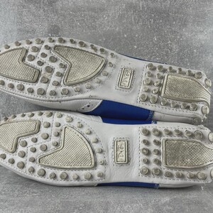 May include: A pair of white and blue leather loafers. The soles are white with small, round, grey rubber studs and textured patches. The blue leather is visible on the sides. The shoes have the "D&G" logo.
