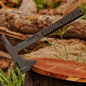 May include: A matte black tactical tomahawk featuring a sharp, pointed spike on the rear of the head and a textured, grooved handle secured with three visible screws. The tool has a sleek, uniform dark finish and a balanced, angular design.