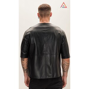 May include: A black leather short-sleeved shirt with a round neckline. The shirt has a panel design and is made of a smooth, textured material.