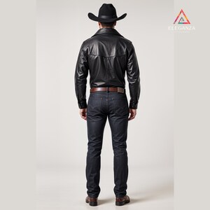 May include: A black leather jacket, dark wash jeans, and a black cowboy hat. The jacket has a button-down front and a brown belt. The outfit is completed with brown leather boots. The Elegenza logo is in the upper right corner.