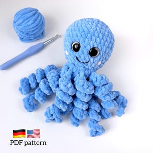 May include: A light blue crochet octopus plush toy with large black safety eyes and a stitched smile. Beside the plush are a matching ball of blue yarn and a blue crochet hook. The image includes the text PDF pattern with German and US flags.