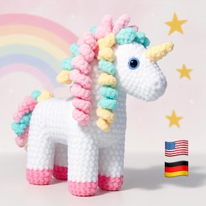 May include: A white crocheted unicorn with a yellow horn, blue eyes, and a colorful mane and tail. The mane and tail feature pink, blue, and yellow yarn. The unicorn has pink hooves and is set against a background with a rainbow and stars.
