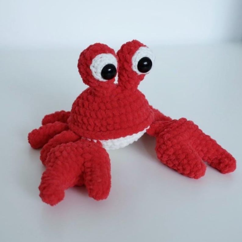 May include: A red crocheted crab with white eyes and a white belly. The crab is a plush toy.