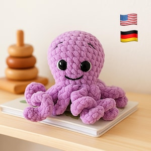 May include: A lavender crochet octopus toy with large black eyes and a smiling face. The octopus is placed on a book, with a wooden stacking toy in the background. The plush toy is a soft, cuddly item, perfect for children.