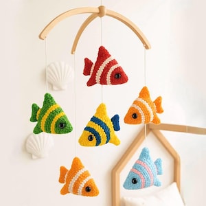 May include: A colorful baby mobile featuring six crocheted fish in various colors, including red, green, yellow, orange, and blue. The fish are suspended from a wooden arch. The mobile is designed to hang above a crib or bed.
