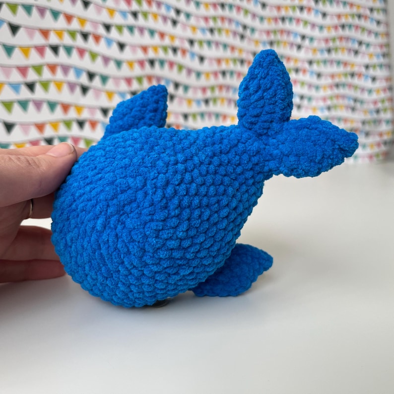 May include: A blue crocheted whale plush toy. The whale is made with a textured yarn that gives it a fuzzy appearance.