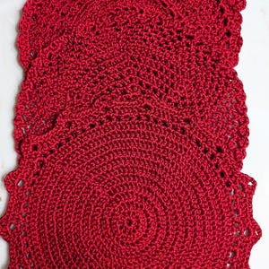 Può includere: Tre tovagliette all'uncinetto rosse con bordo smerlato.