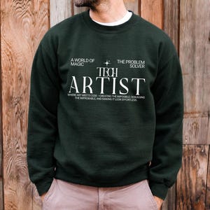 May include: A dark green crewneck sweatshirt featuring white text that reads A WORLD OF MAGIC, THE PROBLEM SOLVER, TECH ARTIST, and WHERE ART MEETS CODE—CREATING THE IMPOSSIBLE, DEBUGGING THE IMPROBABLE, AND MAKING IT LOOK EFFORTLESS.