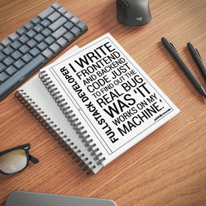 a spiral notebook with a quote on the cover, a keyboard, a mouse, and a pair of glasses on a wooden desk.
