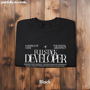 A black t-shirt with white text printed on it, laid out on a wooden surface.