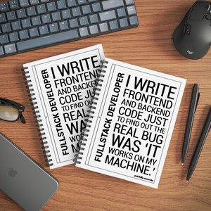 two spiral notebooks with text printed on them, placed on a wooden surface alongside a computer keyboard, mouse, and pens.
