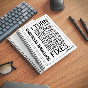 a notebook with a humorous quote about software development, accompanied by a keyboard, mouse, and other office supplies on a wooden desk.