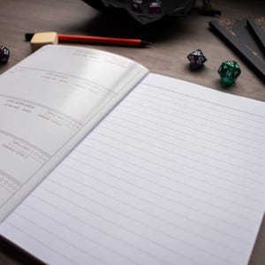 an open notebook with blank lined pages, a pen, and two dice on a wooden surface.