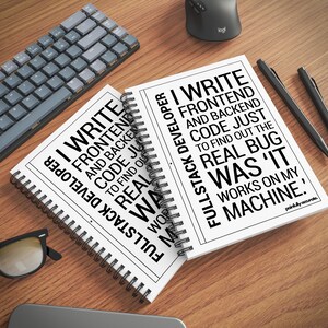 two spiral notebooks with text printed on them, placed on a wooden surface alongside a keyboard, a mouse, and a pair of glasses.
