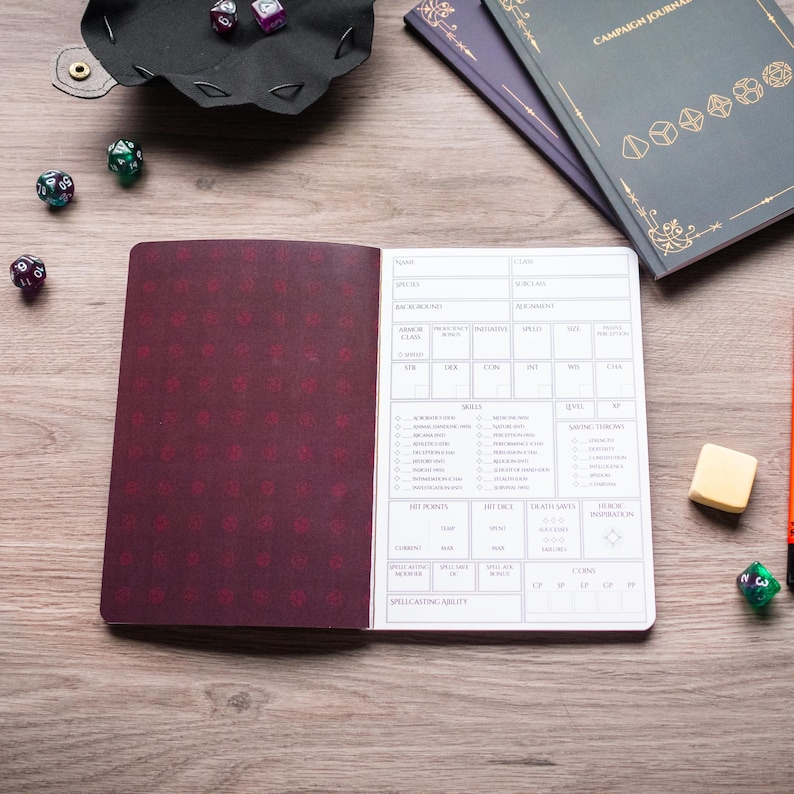 a book with a detailed inventory sheet, a black tray with dice, and various other items such as a pen and a small object on a wooden surface.
