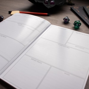 An open notebook with blank pages, a pen, and two dice on a wooden surface.