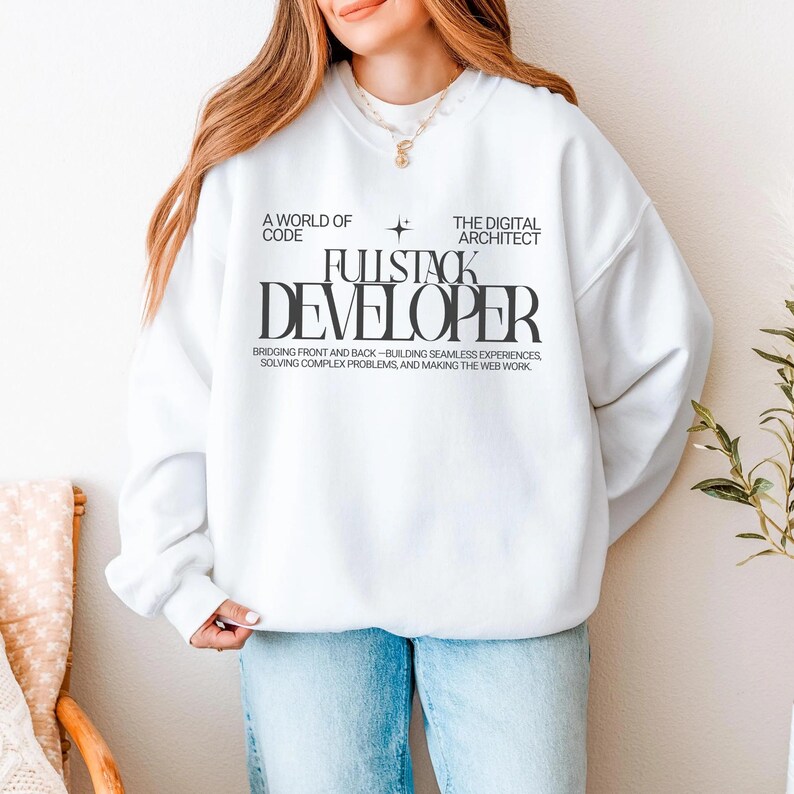 A woman wearing a white sweatshirt with text printed on it stands in front of a white wall, with a potted plant to her right.