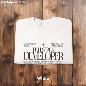A white t-shirt with text printed on it, laid out on a wooden surface.