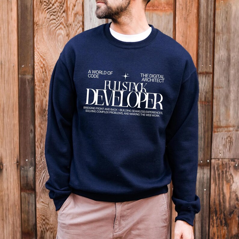 A man wearing a navy blue sweatshirt with white text on it, standing in front of a wooden wall.