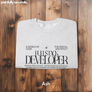 A white t-shirt with black text printed on it, laid out on a wooden surface.