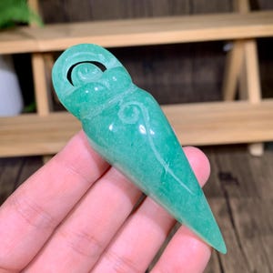 Peut inclure: Un pendentif en pierre verte sculpté en forme de femme avec un motif en spirale.
