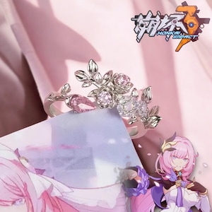 May include: A silver ring with a floral design featuring pink and white crystals. The ring is set against a pink background with the text "Honkai Impact" visible in the upper right corner.