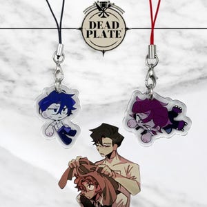 Op de afbeelding: Twee anime-achtige karaktercharms met zwarte en rode lanyards. De charms zijn gemaakt van helder acryl en tonen een blauwharig personage met een wit shirt en een zwarte broek en een paarsharig personage met een wit shirt en een zwarte broek. De charms hangen aan een wit oppervlak met de tekst "DEAD PLATE" in zwart.