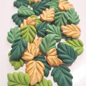 Könnte beinhalten: Eine Sammlung von blattförmigen Verzierungen in verschiedenen Grün- und Goldtönen. Die Blätter sind zusammengelegt, mit einer Mischung aus hellgrünen, dunkelgrünen und goldfarbenen Blättern. Diese dekorativen Blätter eignen sich für Bastelarbeiten und andere kreative Projekte.