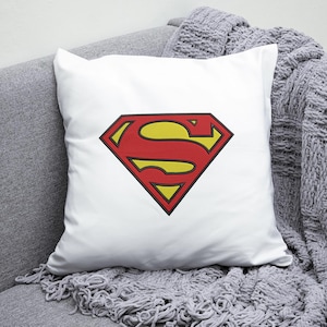 May include: White pillow with a red and yellow Superman logo. The logo is a stylized 'S' inside a diamond shape.
