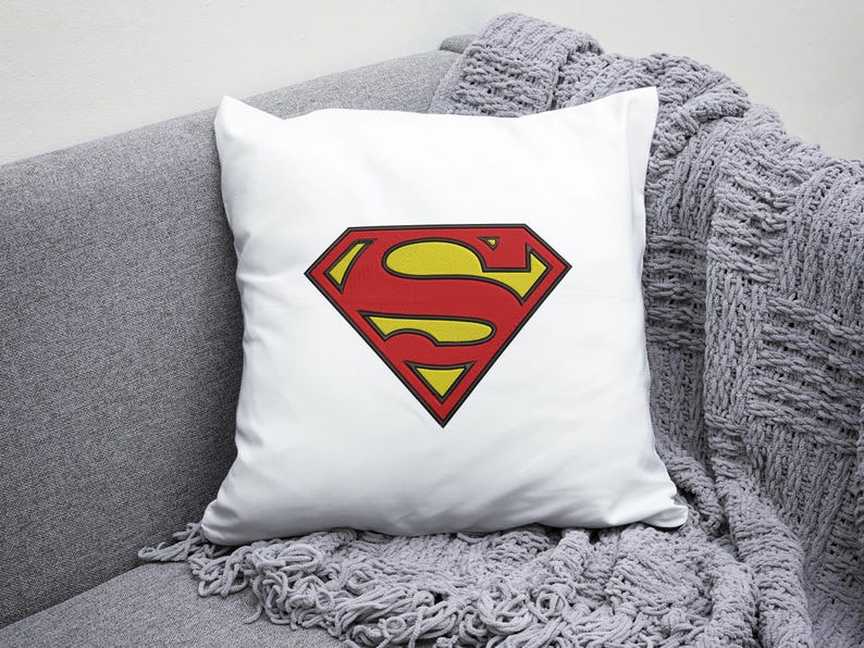 May include: White pillow with a red and yellow Superman logo. The logo is a stylized 'S' inside a diamond shape.