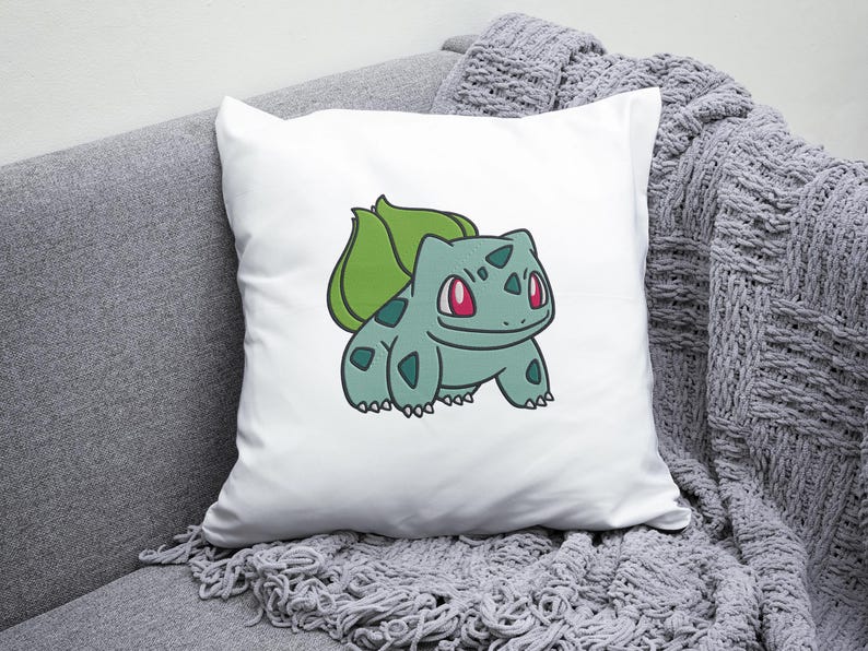 May include: White pillow with a green and blue cartoon image of a Pokemon character, Bulbasaur, with red eyes. The character is on a white background.