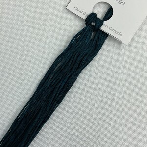 May include: A skein of dark teal embroidery floss labeled "Storm Surge" with a length of 7.5 meters or 8.2 yards. The floss is hand-dyed and attached to a white tag.