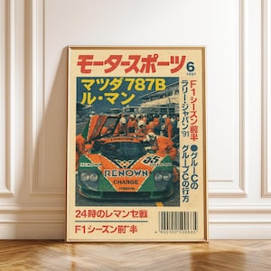 Puede incluir: Un póster vintage enmarcado con un coche de carreras Mazda 787B en naranja y verde. El texto japonés se muestra en la parte superior e inferior, con texto adicional en el lado derecho. El póster está en un marco dorado.