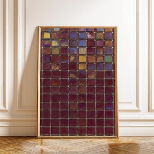 Può includere: Un'opera d'arte incorniciata con un mosaico di piccole piastrelle quadrate. Le piastrelle sono principalmente di un colore bordeaux intenso, con macchie iridescenti di blu, oro e viola. La cornice è sottile, color oro, e l'opera è esposta contro un muro bianco.