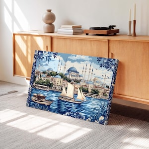 May include: A canvas print depicting a cityscape with blue domes, minarets, and buildings along a waterway. Two boats sail on the water. The print has a blue and white floral border. The sky is blue with clouds.