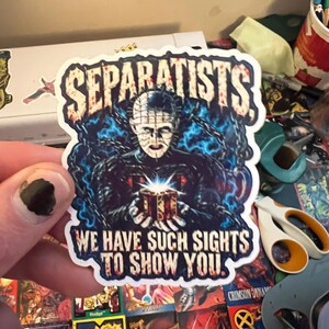 May include: A die-cut sticker featuring a pale, pin-headed figure in a black outfit surrounded by blue chains, holding a glowing puzzle box. The text SEPARATISTS appears at the top, and WE HAVE SUCH SIGHTS TO SHOW YOU is printed at the bottom.